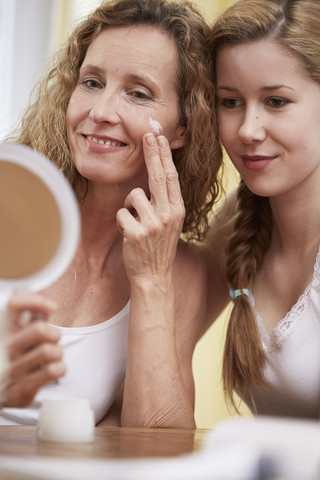 Mutter trägt Gesichtscreme auf ihr Gesicht auf, während Tochter schaut, lizenzfreies Stockfoto