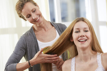 Mother brushing the hair of her daughter at home - STKF001068