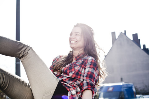 Lachende junge Frau, die sich auf einem Autodach amüsiert, lizenzfreies Stockfoto