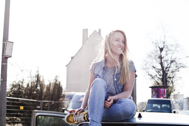 Smiling young woman sitting on car roof - FEXF000086