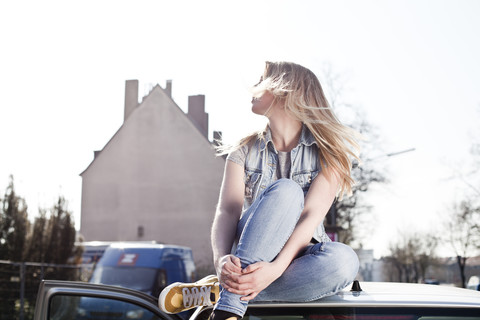 Junge Frau auf dem Autodach sitzend, lizenzfreies Stockfoto