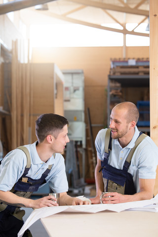 Zwei Handwerker mit Metallbechern im Gespräch, lizenzfreies Stockfoto