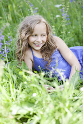 Porträt eines lächelnden Mädchens, das auf einer Blumenwiese liegt - MAEF008559
