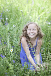 Portrait of smiling girl sitting on flower meadow - MAEF008560