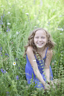 Porträt eines lächelnden Mädchens, das auf einer Blumenwiese sitzt - MAEF008560