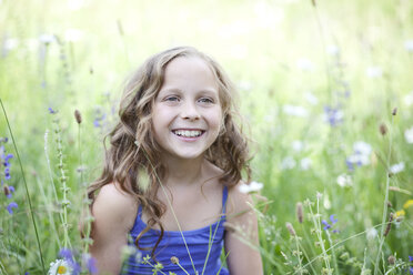 Portrait of smiling girl sitting on flower meadow - MAEF008561