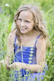 Porträt eines lächelnden Mädchens, das auf einer Blumenwiese sitzt - MAEF008562