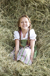 Deutschland, Bayern, Mädchen im traditionellen Dirndl sitzt im Heu - MAEF008565