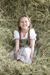 Germany, Bavaria, Girl in traditional dirndl sitting in hay - MAEF008565