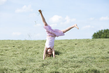 Germany, Bavaria, Young girl doing a cartwheel on meadow with hay - MAEF008570