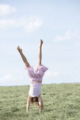 Germany, Bavaria, Young girl doing a handstand on meadow with hay - MAEF008571