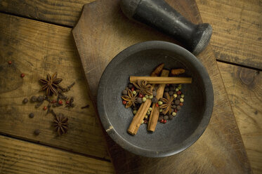 Mortar with dried peppercorns, star anise and cinnamon sticks on wood, elevated view - ASF005438