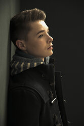 Profile of serious looking teenager leaning against black wall - UUF001196