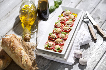 Slices of mozzarella cheese, tomatoes and basil herb on white plate - MAEF008676