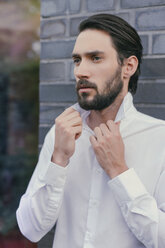 Portrait of young man folding up the collar of his shirt - MFF001145