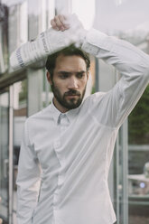 Portrait of young bearded man with newspaper leaning against window pane - MFF001152