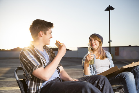 Fröhliche Teenager essen und trinken auf einem Parkplatz, lizenzfreies Stockfoto