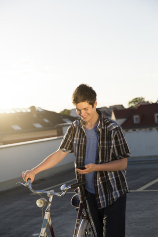 Jugendlicher mit Fahrrad und Mobiltelefon auf einem Parkplatz, lizenzfreies Stockfoto