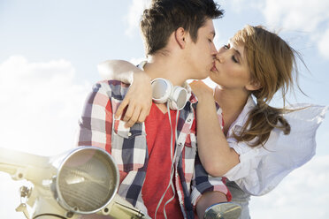 Teenage couple kissing on motor scooter - FKF000599