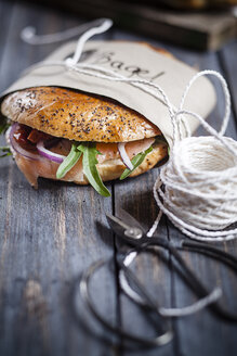 Zwei garnierte selbstgebackene Brötchen, eingewickelt in Papier, Schnur und Schere auf grauem Holz - SBDF000961