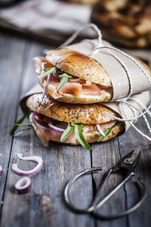 Zwei garnierte selbstgebackene Brötchen in Papier eingewickelt und Schere auf Holz - SBDF000962