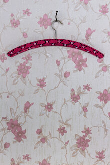 Kleiderbügel mit einem gebogenen Nagel befestigt, der an einer Tapete mit rosa Blumenmuster hängt - EJWF000407