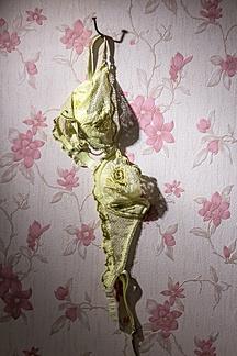 Yellow bra hanging on bent nail in front of wallpaper with pink floral  design stock photo