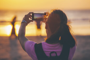 Indonesien, Bali, Frau am Strand beim Fotografieren des Sonnenuntergangs mit ihrem Smartphone - EBSF000253