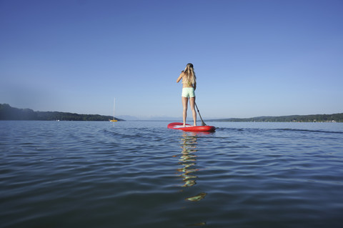 Deutschland, Bayern, junge Frau stehend auf Stand Up Paddle Board am Starnberger See, Rückansicht, lizenzfreies Stockfoto