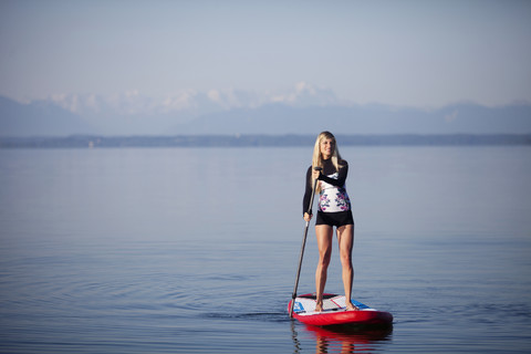 Germany, Bavaria, young woman standing on stand up paddle board at Lake Starnberg stock photo