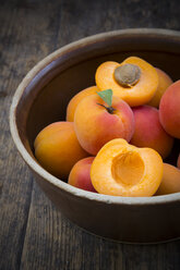 Bowl of sliced and whole apricots on wood - LVF001532