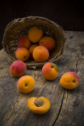 Sliced and whole apricots on wood with basket at the background - LVF001535