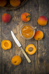 Glass of apricots jam, knife and sliced and whole apricots on wood, elevated view - LVF001537