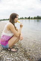 Porträt einer jungen Frau mit Eis am Stiel am Strand - UUF001198