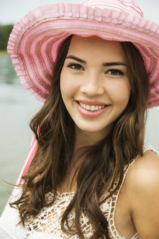 Porträt einer lächelnden jungen Frau am Strand mit rosa Sommerhut, lizenzfreies Stockfoto