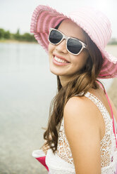 Porträt einer lächelnden jungen Frau mit Sonnenbrille und rosa Hut am Strand - UUF001206