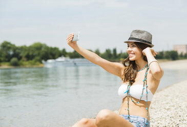 Porträt einer jungen Frau, die am Strand ein Selfie mit ihrem Smartphone macht - UUF001229