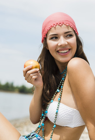 Porträt einer lächelnden jungen Frau mit Apfel am Strand, lizenzfreies Stockfoto