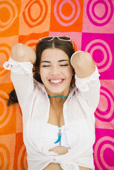 Porträt einer glücklichen jungen Frau auf einem Strandtuch liegend, Ansicht von oben - UUF001297