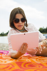 Porträt einer jungen Frau, die auf einem Strandtuch liegt und ein digitales Tablet benutzt - UUF001269