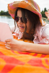 Porträt einer jungen Frau mit Sommerhut und Sonnenbrille, die ein digitales Tablet benutzt - UUF001272