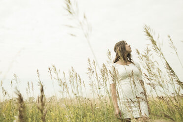 Junge Frau steht auf einer Blumenwiese und schaut in den Himmel - UUF001258
