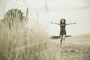 Young womanwith outstretched arms running on a harvested meadow - UUF001321