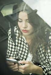 Portrait of young woman sitting in car using her smartphone - UUF001333