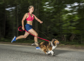 Junge Frau joggt mit Hund auf der Straße - STSF000434