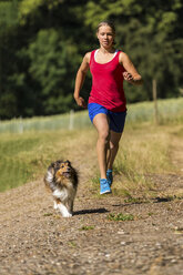 Young woman jogging with dog on field path - STSF000437