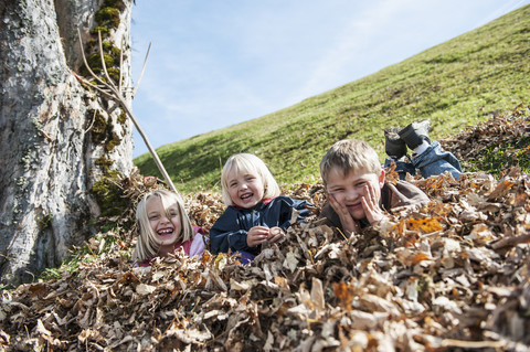 Drei verspielte Kinder im Herbstlaubhaufen, lizenzfreies Stockfoto