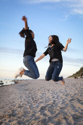 Deutschland, Rügen, Zwei junge Freundinnen springen am Strand - OJF000050