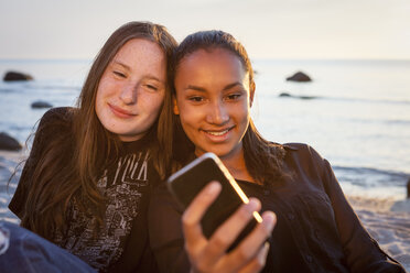 Deutschland, Rügen, Zwei junge Freundinnen mit Smartphone am Strand - OJF000054