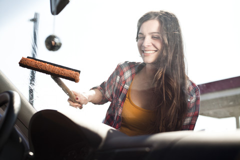 Lächelnde junge Frau beim Reinigen der Windschutzscheibe eines Autos, lizenzfreies Stockfoto